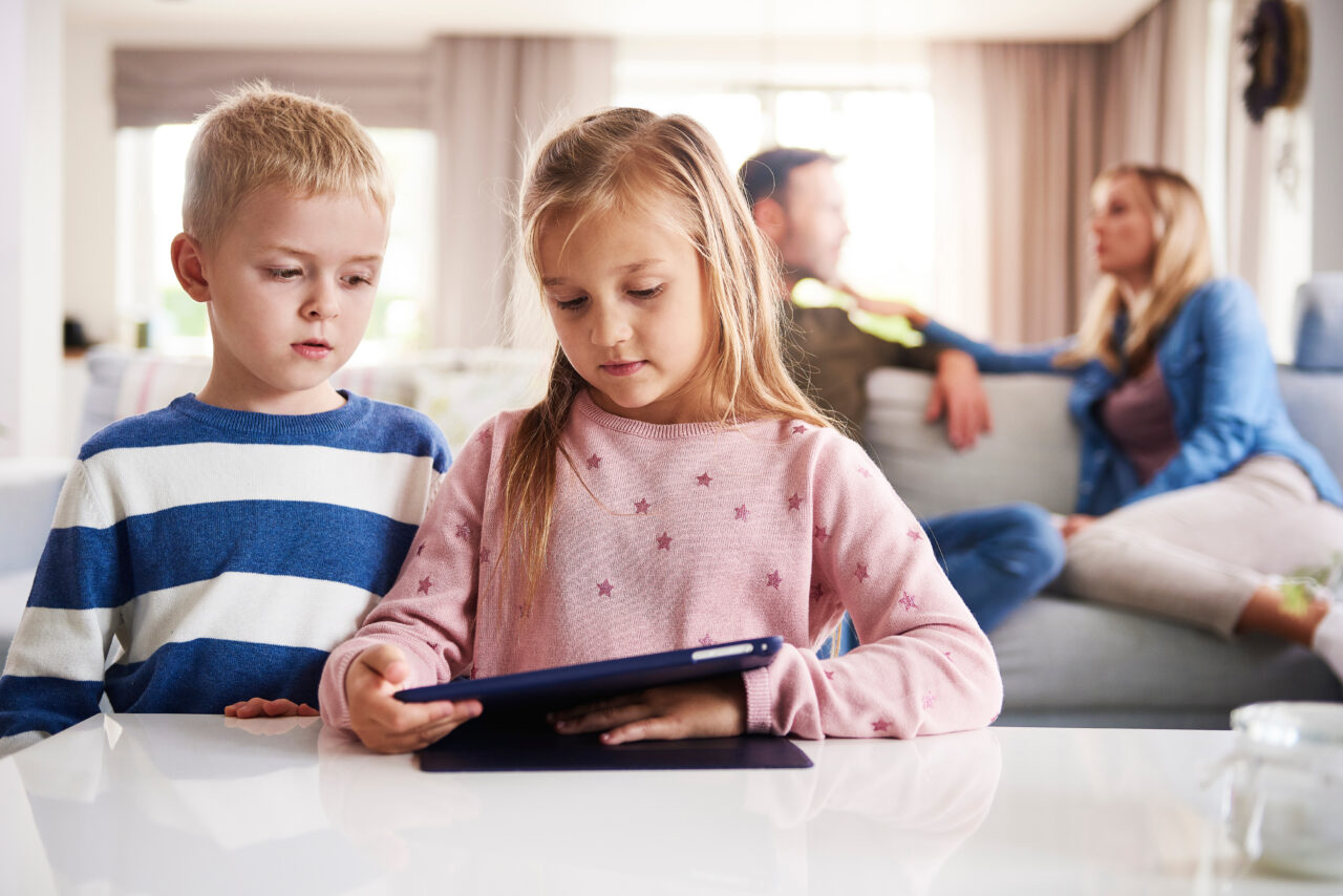 Copyright (c) 2020 gpointstudio/Shutterstock Kinder am Tablet, Eltern verschwommen im Hintergrund zu sehen