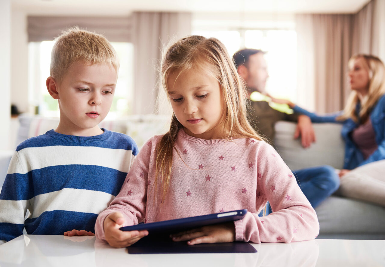 Bildnachweis: gpointstudio / Shutterstock Kinder am Tablet, Eltern verschwommen im Hintergrund zu sehen