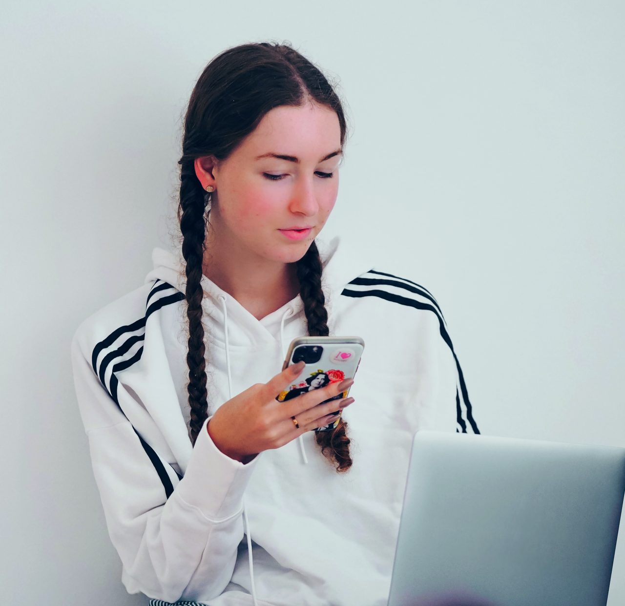 Bildnachweis: Laura Chouette / pexels Eine Jugendliche sitzt auf dem Bett und schaut aufs Handy, während sie einen Laptop auf dem Schoß hat.